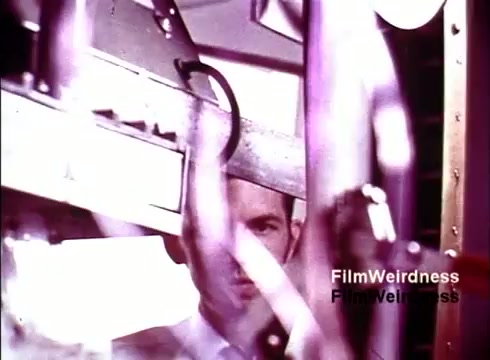 The still from the 16mm film 'Bell Performance' offers a glimpse into the production process of telephones in the 1970s. The image features a man observing machinery, with various mechanical components visible in the foreground. The film captures the nostalgia of the Bell System era, highlighting the intricate and industrial nature of telephone manufacturing. The absence of titles suggests a straightforward documentary style focused on the operations of the time.