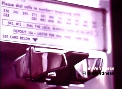 The still from 'Bell Performance' showcases a vintage payphone with a close-up of the dialing mechanism. The background includes a printed instruction panel with dial numbers and some operational details, characteristic of 1970s telecommunications. The color tone appears muted, reflecting the era's aesthetic, evoking nostalgia for the Bell System and its iconic technology. Overall, it captures a moment in time related to phone usage and innovation.