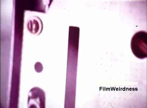 The 16mm still from 'Bell System Film from the 1970s' shows a close-up of machinery, possibly involved in the assembly of telephones. The image captures metallic components, screws, and a slot indicative of manufacturing equipment, conveying a sense of nostalgia for telecommunications technology. The grain and color palette typical of the era enhance the vintage feel, reflecting both the industrial process and the significance of the Bell System in the history of communication.