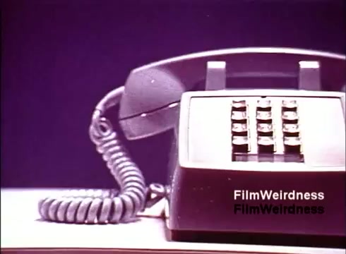 The still features a vintage telephone with a prominent keypad, typical of the 1970s era. The phone, with a coiled cord, is presented against a simple, monochromatic background. The focus on the device emphasizes the craftsmanship and design of telecommunications equipment from that time, capturing a sense of nostalgia related to the Bell System's legacy in telecom innovation. The aesthetic suggests a promotional or educational purpose, highlighting the technology's role in communication.