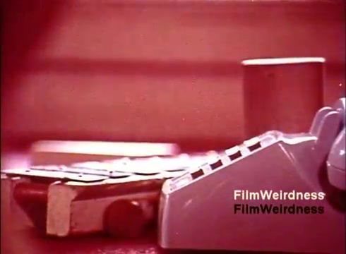 The still from 'Bell System Film from the 1970s' likely features a close-up of a telephone, showcasing the design and features characteristic of that era. The image may capture the textured surface of the phone and possibly other elements like parts or materials involved in the manufacturing process. The color palette appears muted, hinting at the nostalgic feel of the film, aligning with the theme of telecommunication technology during the 1970s. Overall, it reflects an era of innovation and the evolution of communication devices.