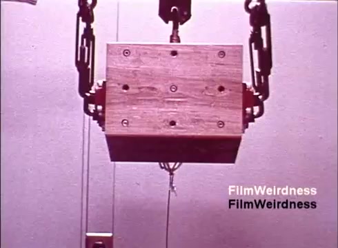The 16mm still from 'Bell System Film from the 1970s' captures a wooden box suspended by a mechanical apparatus. The scene likely represents an industrial process, possibly related to telephone manufacturing. The lack of titles suggests a focus on the visuals of production rather than a narrative. This piece serves as a nostalgic glimpse into the era's technology and manufacturing practices associated with the Bell System.
