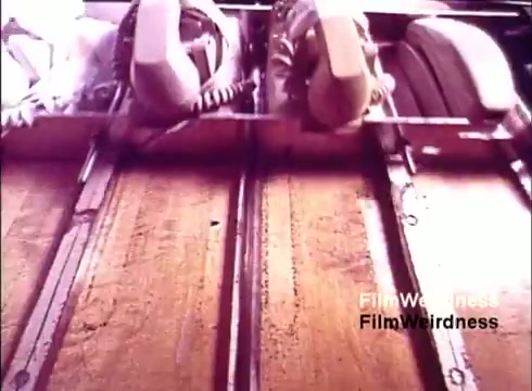 The still from the 16mm film 'Bell Performance' showcases a close-up view of the manufacturing process of telephones. It features rows of telephones being assembled, with the focus on their distinctive earpieces and cords. The setting conveys a sense of nostalgia for the Bell System era, highlighting industrial production and technology from the 1970s. Overall, it captures a moment of technological history related to communication devices.