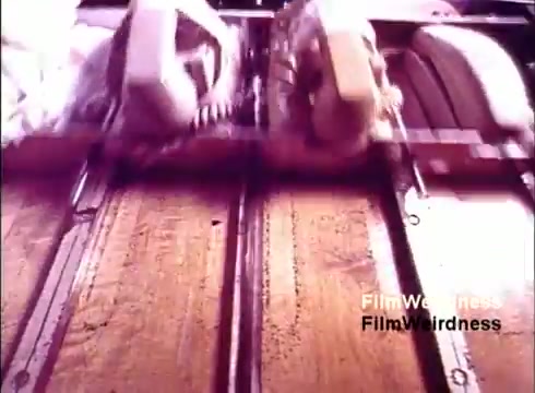 The still from the 16mm film 'Bell Performance' captures an assembly line where telephones are being manufactured. The image focuses on a close-up view, showing the intricate process of creating these devices. The muted, vintage color palette evokes nostalgia for the Bell System era, highlighting the industrial setting and mechanical precision involved in telephone production. The absence of titles emphasizes the raw nature of the film, making it an intriguing piece of historical documentation.