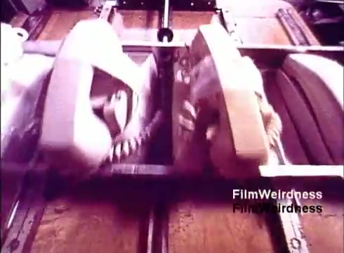 The still captures a moment from the 1970s Bell System film 'Bell Performance.' It features two telephones moving along a production line, showcasing the manufacturing process. The image emphasizes the design and assembly of the phones, highlighting the nostalgia of that era's technology. The muted colors and vintage aesthetic evoke a sense of historical significance related to telecommunications.