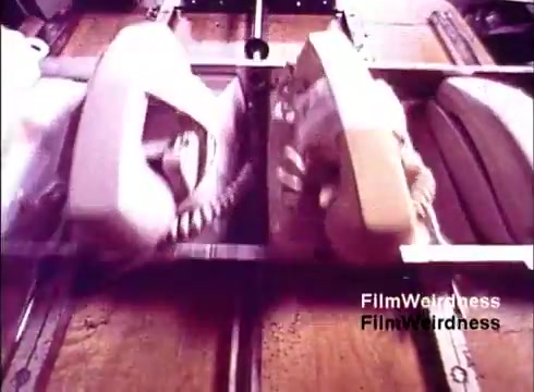 This 16mm still from the 1970s film 'Bell Performance' captures an assembly line scene where telephones are being produced. The image shows multiple telephones in various colors moving along a conveyor belt, highlighting the manufacturing process. This still evokes a sense of nostalgia for the Bell System era, showcasing the technology and design of the time. The absence of titles adds to its enigmatic quality, focusing the viewer's attention on the intricate workings of telephone production.