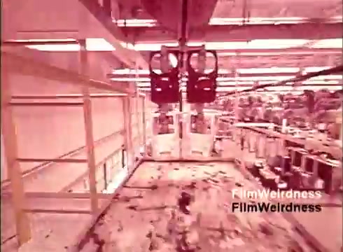 The 16mm still from 'Bell System Film from the 1970s,' titled 'Bell Performance,' features an industrial setting inside a telephone manufacturing facility. The image likely shows automated machinery at work, possibly moving components or finished products through the assembly line. The scene conveys a nostalgic view of technological processes from that era, highlighting the evolution of telecommunications. The color palette may be warm or stylized, characteristic of period films.