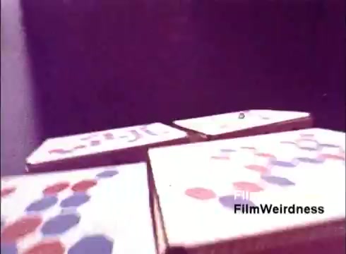 The still from 'Bell Performance' features abstract graphics resembling hexagonal and circular patterns in vibrant colors, prominently red and blue. The composition suggests a focus on design elements typical of telecommunications materials, possibly indicative of the creative processes behind telephone manufacturing. The visual style reflects a nostalgic aesthetic from the 1970s, contributing to the overall allure of Bell System history.