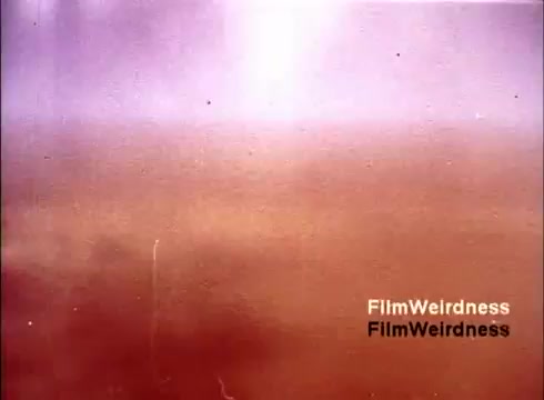 The still from the film 'Bell Performance' showcases a faded and abstract background typical of older 16mm film. The colors appear muted with a blend of purples and browns, suggesting age and wear. There's an organic texture that reflects the film's historical context, likely evoking nostalgia for the Bell System era, despite not depicting any specific telephones or manufacturing processes directly.