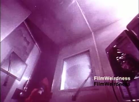 The still from 'Bell System Film' presents an industrial setting, likely related to the manufacturing process of telephones. The scene features muted colors, predominantly purples, giving it a nostalgic and somewhat surreal vibe. In the background, you can spot equipment and a window, suggesting a controlled environment, possibly a lab or factory setting. This captures a moment in the production of telecommunications technology during the 1970s. The overall ambiance evokes a sense of history and innovation from the Bell System era.