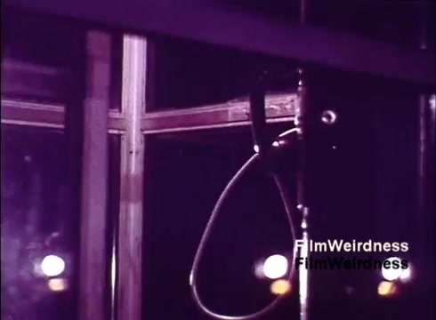 The still from 'Bell System Film from the 1970s' features a close-up of a vintage telephone in a glass display or manufacturing area. The image captures the essence of telecommunication history, showcasing the design and craftsmanship of the time. Dim lighting accentuates the reflective surfaces, creating a nostalgic atmosphere reminiscent of the era's technological advancements. Overall, it evokes feelings of nostalgia and curiosity about the evolution of telephony.