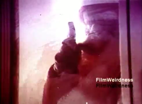 The 16mm still from 'Bell System Film from the 1970s' depicts a close-up shot of a worker in a phone manufacturing environment, possibly involved in assembling or inspecting telephones. The image captures the nostalgia of the era, showcasing the processes and technology related to telephone production. The color tones and composition likely evoke a sense of industrial history and the significance of the Bell System in telecommunications.