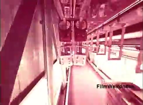 The 16mm still from 'Bell Performance' features a unique industrial setting, likely showcasing the inner workings of a telephone manufacturing process. The image is characterized by a retro, slightly faded aesthetic typical of 1970s film, with elements such as machinery, assembly lines, and possibly telecommunication equipment. The scene gives a nostalgic glimpse into the era of the Bell System, emphasizing innovation in telecommunications. The overall tone is intriguing, reflecting the period’s fascination with technology and production.