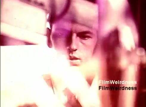 The still from 'Bell Performance' captures a moment in a 1970s film focused on the manufacturing process of telephones. It features a worker intensely focused on his task, framed behind various industrial elements. The lighting gives a slightly surreal quality, with soft colors creating an ethereal ambiance. This snapshot evokes nostalgia for the era's technology and craftsmanship, reflecting the intersection of human effort and innovation in telecommunications.