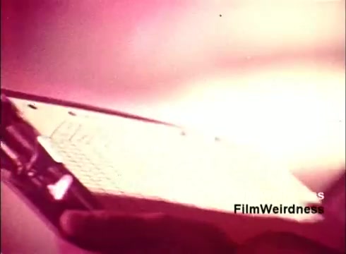 The still from the film 'Bell Performance' features a close-up of a clipboard with notes or plans, partially obscured by a hand. The lighting creates a warm, nostalgic glow, reflecting the vintage aesthetic of the 1970s. This scene likely captures a moment related to the production or design processes involved in creating telephones, evoking a sense of nostalgia for the Bell System era.