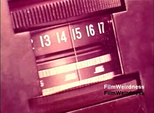 The still from the 'Bell System Film from the 1970s' shows a close-up view of a mechanical counter or a dial, likely used in the production or testing of telecommunication equipment. The numbers range from 13 to 17, indicating a measurement or counting function. The overall aesthetic has a vintage feel, reflecting the era's technology and design. This moment captures the intricate workings behind telephone manufacturing, contributing to the nostalgia associated with the Bell System.