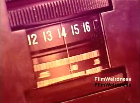 The 16mm still appears to show a close-up of a dial or gauge, likely related to telecommunications equipment from the 1970s. The numbers 12 to 16 suggest it could be part of a measuring device. The color palette hints at vintage aesthetics typical of that era. This still evokes a sense of nostalgia linked to the Bell System and its technological advancements during that time.