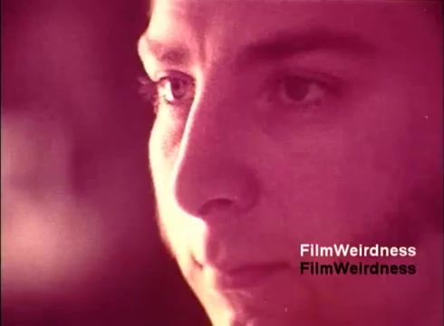 The still from the 16mm film 'Bell Performance' features a close-up of a young man, capturing a thoughtful expression. The image has a warm, vintage aesthetic typical of the 1970s, with a predominant reddish tone. The focus appears to be on the individual's eyes, conveying a sense of concentration or contemplation. The context suggests a connection to the Bell System, potentially highlighting the human elements behind the development of telephone technology during that era.