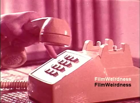 The still from 'Bell Performance' features a close-up of a vintage telephone handset being used, with a hand dialing the keys on a distinctive beige telephone base. The soft, pink-tinted color palette adds a nostalgic feel, typical of 1970s design. The absence of titles underscores its documentary-style presentation, focusing on the everyday use and design of telephonic technology from the era, evoking a sense of nostalgia for the Bell System.