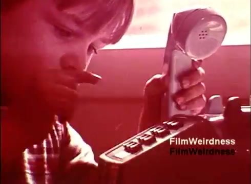 The still from the 1970s Bell System film, 'Bell Performance,' features a close-up of a young child interacting with a telephone. The image presents a nostalgic view of telecommunications, capturing the child's focused expression as they examine the device. The scene likely emphasizes the craftsmanship involved in phone manufacturing, showcasing a mix of curiosity and technological heritage. The color palette suggests a warm, vintage aesthetic typical of that era.