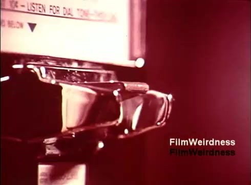 The still from the 16mm film 'Bell Performance' features a close-up of a payphone, highlighting its design and components. The image is imbued with a nostalgic vibe, reflecting the era of the 1970s. The film focuses on the creation and functionality of telephones within the Bell System, capturing a slice of technological history. The lighting adds a warm tone, enhancing the vintage aesthetic.