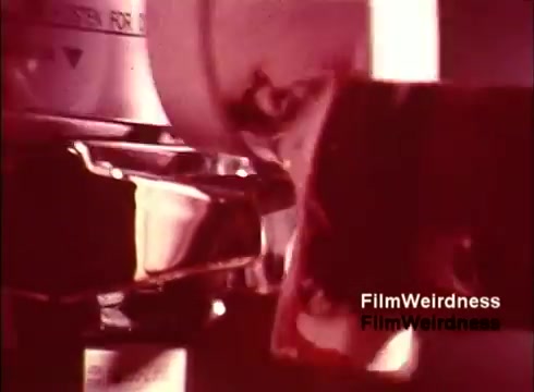 The still from the 'Bell System Film' captures a close-up of a vintage telephone being assembled or manufactured. The image likely displays intricate machinery and parts involved in the production process, reflecting the nostalgia of the 1970s era in telecommunications. The warm color tones enhance the retro feel, emphasizing the craftsmanship and technology of that time.