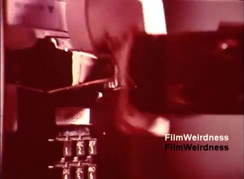 The still appears to capture a moment from a 16mm film focused on the production of telephones, likely emphasizing the manufacturing process. The image showcases machinery at work, possibly illustrating the intricate technology behind telephone systems, with a vintage aesthetic characteristic of the 1970s. The film likely serves as a nostalgic glimpse into the Bell System's operations during that era.