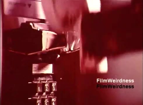 The still from 'Bell Performance' features a close-up of a telephone, likely a payphone, showcasing its keypad and receiver. The image has a warm, faded color palette typical of 1970s film, emphasizing a nostalgic aesthetic. This focus suggests a moment in the manufacturing process or usage, highlighting the design and functionality of Bell System telephones during that era. The absence of titles enhances the film's documentary feel, immersing viewers in the culture and technology of the time.