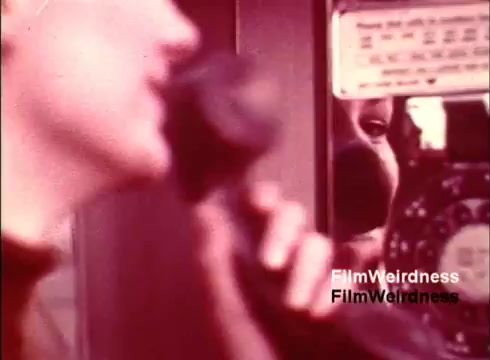 The still from 'Bell Performance' captures a moment in the 1970s where a person is using a classic telephone, with a focus on a rotary dial. The composition emphasizes the interaction between the user and the phone, highlighting the nostalgia of the era's communication technology. The color palette suggests a vintage aesthetic, enhancing the retro feel of the film. The overall vibe conveys an exploration of telephone innovation and usage during a significant period in telecommunications history.