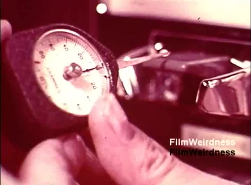 The still from the 'Bell System Film from the 1970s' captures a close-up of a person's hand holding a gauge or timer, likely measuring a specific process related to telephone manufacturing. The background suggests a workshop or manufacturing setting, emphasizing the technical aspects of telephone creation. The overall tone reflects a nostalgic glimpse into the era of Bell System's technological advancements.
