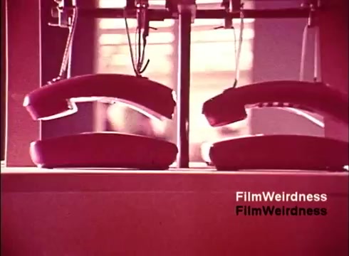 The still from 'Bell System Film from the 1970s' showcases a close-up view of two partially assembled telephone handsets. The image is saturated with hues of pink and red, reflecting the aesthetic of the era. It captures a moment in the manufacturing process, highlighting the intricate details of telephone design. The overall mood conveys a sense of nostalgia for the technology and innovation of the time, embodying the spirit of the Bell System's legacy.