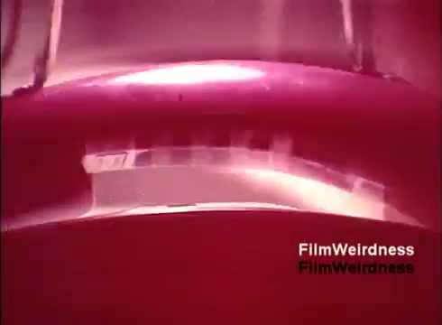 The still from 'Bell Performance' likely showcases a close-up of a manufacturing process, possibly depicting a telephone component being crafted. The color palette features dominant shades of red and pink, creating a nostalgic and somewhat surreal ambiance. The abstract framing could highlight the intricacies of the assembly line, emphasizing the technology of the era while invoking memories of the Bell System's history. Overall, it captures the essence of vintage industrial filmmaking, focusing on progress and innovation in telecommunications.