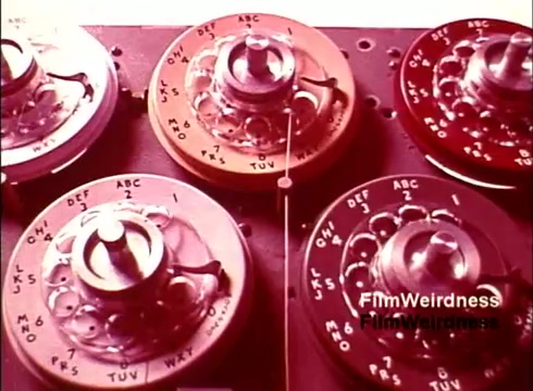 The still features a close-up view of rotary phone dials, highlighting the intricate design and technology of telecommunication equipment from the 1970s. The dials are labeled with letters and numbers, reflecting the era's classic telephone interface. The overall aesthetic showcases a blend of nostalgia and technical craftsmanship, representative of the Bell System's heritage in telecommunications. The color palette is warm, adding to the vintage feel of the film.