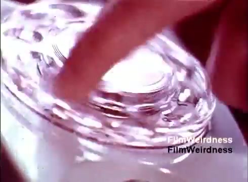 The still from the 'Bell System Film from the 1970s' captures a close-up of a hand interacting with a classic rotary telephone. The focus highlights intricate details of the phone’s design, showcasing how the device operates. This image evokes a sense of nostalgia, reflecting the craftsmanship and technology of the era, as well as the importance of telecommunication in daily life during that time. The scene emphasizes the tactile experience of using such devices, which contrasts sharply with today's digital technology.