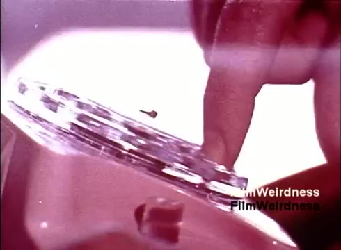 The still from the 'Bell System Film from the 1970s' captures a close-up of a hand pressing a button on a rotary telephone. The vibrant colors and retro aesthetic evoke a sense of nostalgia for the era, highlighting the craftsmanship and technology of telecommunication at the time. The focus on the interaction emphasizes the tactile experience of using telephones before the digital age took over.