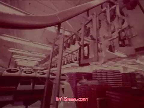 The still from the 16mm film 'Performance' (Bell System Film, 1971) features a factory or industrial setting, showcasing rows of equipment and machinery against a backdrop of organized stacks. The overall color tone appears muted, likely giving a vintage feel common in 16mm prints. This segment includes the end titles, listing the production date, cast, and crew involved in the film's creation, contributing to the film's historical context.