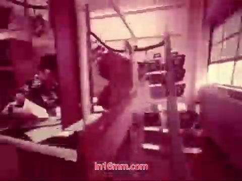 The still from 'Performance' (Bell System Film, 1971) features a scene likely set in a workshop or studio environment, with various technical equipment and individuals engaged in activities. The overall color tone suggests a vintage aesthetic typical of 16mm film, possibly with a reddish hue. The composition includes elements like machinery or tools and perhaps a window allowing natural light to filter in. This context serves as a visual bridge to the concluding titles, which provide details about the production date and the cast and crew involved.