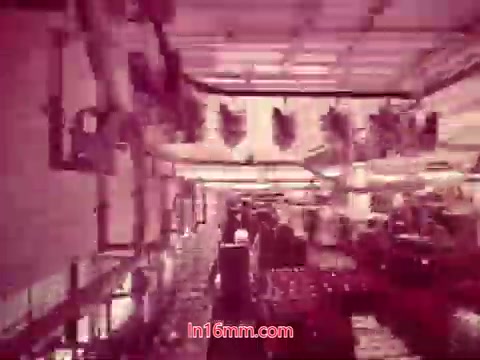 The still depicts a stylized scene from the 16mm film 'Performance' produced by Bell System in 1971. The image features a busy interior space, possibly a factory or workshop, with various industrial elements visible. The colors appear muted with a reddish hue, characteristic of older film prints. The end titles are likely visible, providing production details, cast and crew information, and the production date. This captures the essence of the film's themes related to technology and performance.