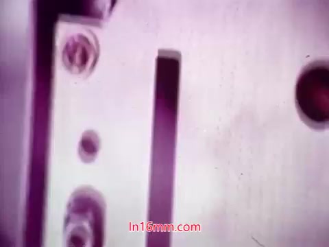 The still from the 16mm film 'Performance' is a close-up shot, likely showing part of a film projector or film reel. The image features metallic components, possibly including screws and film slots, with a purple hue that suggests a vintage aesthetic. This frame encapsulates the film's end titles, indicating production details and crediting the cast and crew. The overall tone of the image conveys the charm of analog film.