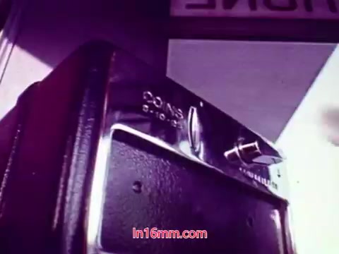 The 16mm still from 'Performance' showcases a close-up of a coin-operated device, likely a film projector or viewer, with a distinctive shiny surface. The background is somewhat blurred, suggesting a focus on the device and its functional details. The scene may evoke a sense of nostalgia or a retro aesthetic, characteristic of films from the early 1970s. This still likely serves as part of the film’s end credits, summarizing the production details and contributing to the overall thematic feel of the piece.