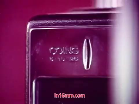 The still features a close-up shot of a coin slot on a device, likely a vending machine or payphone. The date “9-10-25” is marked near the slot. The image has a vibrant color palette, typical of 16mm films from the era. This shot captures a detail relevant to the film's context, possibly emphasizing themes of money or transactions reflective of its time.