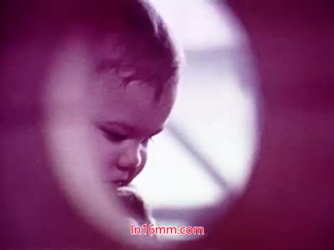 The still features a close-up of a child's face, depicted through a circular frame that adds a soft focus around the edges. The child's expression appears contemplative, with the light casting gentle shadows, creating an intimate atmosphere. The color palette consists of warm hues, contributing to a nostalgic or dreamlike quality that is characteristic of the film's overall aesthetic. The context portrays a moment that might evoke emotion or reflection, fitting within the narrative scope of 'Performance.'