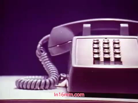 The still from the 16mm film 'Performance' features a classic desk phone, prominently displayed with a coiled cord. The focus is on the phone's keypad, which has eight buttons. The background appears muted to draw attention to the phone, reflecting the film's vintage aesthetic. This still likely marks the film's end titles and mentions details such as the production date and credits for the cast and crew, encapsulating a moment of nostalgia and significance in the film's narrative.