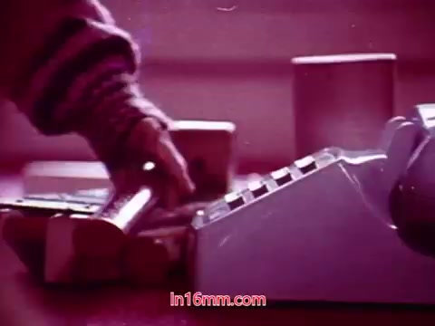 The still from 'Performance' - Bell System Film (1971) features a close-up of a hand reaching for an object, possibly a receiver, next to a large, retro-styled telephone. The color palette appears warm, with pinkish tones, creating a nostalgic atmosphere. This moment captures the tactile interaction with technology from that era, fitting within the context of the film's exploration of communication. The end titles indicate production details, including the date and credits for the cast and crew.