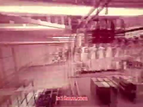 The still from the 16mm film 'Performance' - Bell System Film (1971) depicts a mechanical and industrial setting, likely representative of telecommunications equipment. The image showcases a series of machinery, possibly within a factory or processing area, with prominent lines and geometric shapes creating a sense of depth. The overall color tone appears to have a reddish hue, typical of aged film prints. The end titles visible in this frame include production details, highlighting the date and credits for the cast and crew involved in the film.