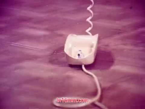 The still from 'Performance,' a 1971 Bell System film, features a close-up of a rotary telephone sitting on a surface. The phone is cream-colored, and a spiraled cord extends from it. The lighting gives the image a purplish hue, setting a unique tone. This shot likely represents a moment of significance related to communication, aligning with the film's themes. The end titles provide credits and production date, marking the completion of the film's presentation.