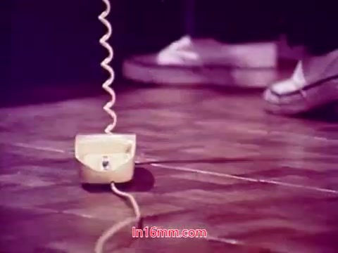 The still from the 16mm film 'Performance' (1971) features a close-up of a retro telephone resting on the floor, with a coiled cord extending from it. The background appears slightly blurred, focusing attention on the phone. The muted colors and lighting contribute to a nostalgic ambiance. This image likely serves as part of the film's end titles, showcasing the production details, cast, and crew.