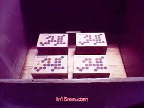 The still from the film 'Performance' features a close-up shot of four boxes arranged in a wooden crate. Each box has a distinct pattern of colored dots. The lighting suggests a warm, nostalgic atmosphere typical of 16mm films, emphasizing the textures of the wood and the boxes. This scene likely serves as part of the film's thematic exploration of communication, production, or presentation, aligning with its context as a Bell System film from 1971. The end titles convey essential production information, including the date and credits for the cast and crew.