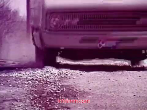 The still from the 16mm film 'Performance' - Bell System Film (1971) features a vehicle moving over a gravel road, accentuated by a cloud of dust being kicked up. The colors have a vintage, muted quality, likely influenced by the film stock and processing of the time. The frame captures a sense of motion, with the focus on the vehicle, hinting at the themes of progress or transition explored in the film. The end titles provide production details, including the date and names of the cast and crew.