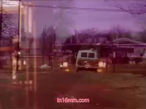 The still from the 16mm film 'Performance' (Bell System Film, 1971) showcases a slightly blurred scene with a van driving through a somewhat desolate outdoor area. The colors appear muted with a blend of earthy tones and a purple hue, enhancing the surreal quality of the image. This frame likely includes elements signaling the end of the film, including production details and credits, capturing the essence of the late 20th-century filmmaking style.